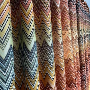 May include: Close-up of a fabric with a chevron pattern in shades of orange, yellow, brown, and blue. The fabric is woven and has a textured surface.