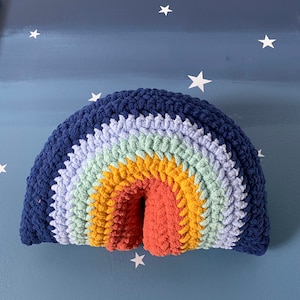 Könnte beinhalten: Ein gehäkeltes Regenbogenkissen in Blautönen, Grün, Gelb, Orange und Rot. Das Kissen ist regenbogenförmig und hat eine weiche, flauschige Textur.
