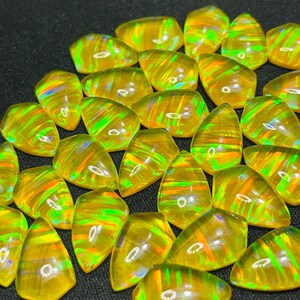 May include: A collection of loose, teardrop-shaped yellow opals featuring a vibrant play-of-colour with flashes of neon green, orange, and red. Each polished gemstone displays a smooth, domed surface with internal light reflections.