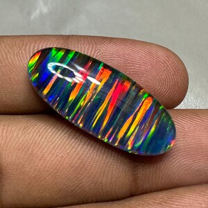 May include: A vibrant, multi-colored opal cabochon with a striped pattern. The opal is oval shaped and has a dark blue, green, orange, and red color scheme.