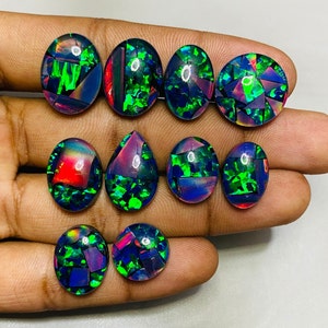 Peut inclure: Une collection de neuf cabochons d'opale noire de forme ovale et en goutte avec des reflets iris&eacute;s verts, bleus et rouges. Les opales sont dispos&eacute;es sur une main.