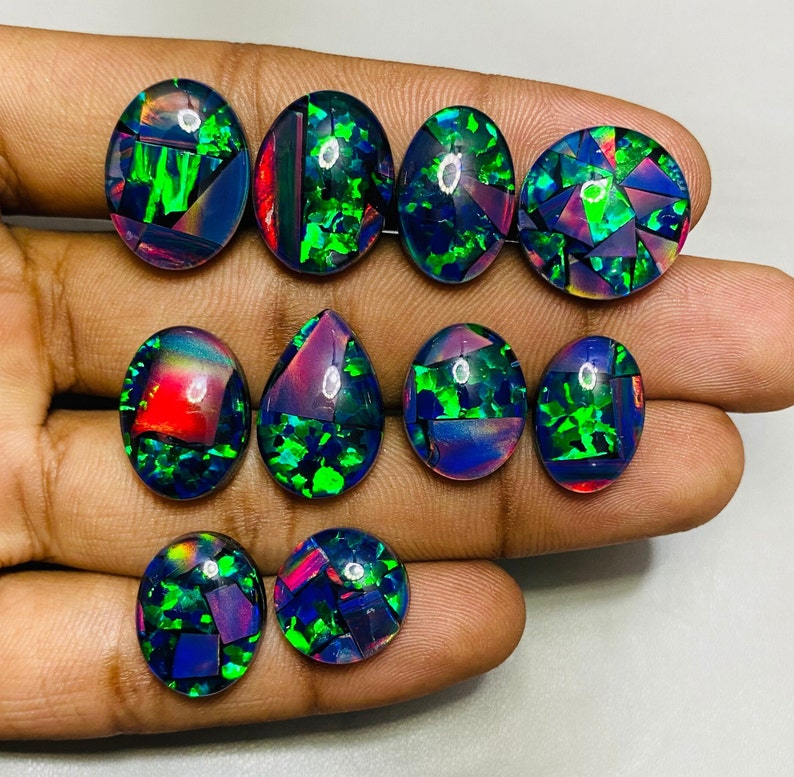 Peut inclure: Une collection de neuf cabochons d'opale noire de forme ovale et en goutte avec des reflets iris&eacute;s verts, bleus et rouges. Les opales sont dispos&eacute;es sur une main.