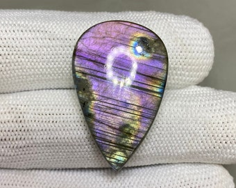 May include: A teardrop-shaped labradorite gemstone with iridescent purple, blue, and green hues. The stone is polished and has a smooth, glossy finish.