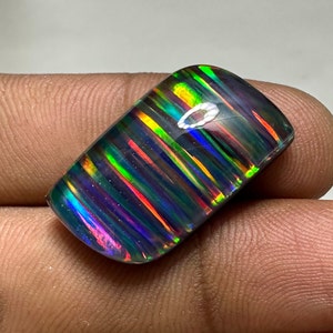 Op de afbeelding: Een donkere, iriserende opaal cabochon met een gestreept patroon van groen, blauw, rood en geel. De opaal heeft een glad, gepolijst oppervlak.