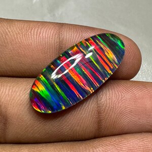 May include: A colorful, iridescent opal cabochon with a striped pattern in shades of red, orange, green, blue, and black. The opal is oval-shaped and has a smooth, polished surface.