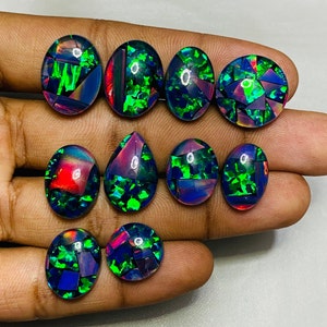 Peut inclure: Une collection de dix cabochons d'opale noire de forme ovale et en goutte avec des reflets iris&eacute;s verts et violets. Les pierres sont serties en mosa&iuml;que.