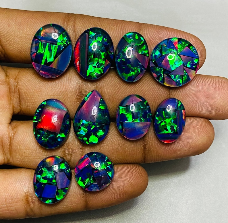 Peut inclure: Une collection de dix cabochons d'opale noire de forme ovale et en goutte avec des reflets iris&eacute;s verts et violets. Les pierres sont serties en mosa&iuml;que.