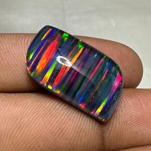 Op de afbeelding: Een zwarte opaal cabochon met een gestreept patroon van iriserende kleuren, waaronder rood, oranje, geel, groen, blauw en paars.
