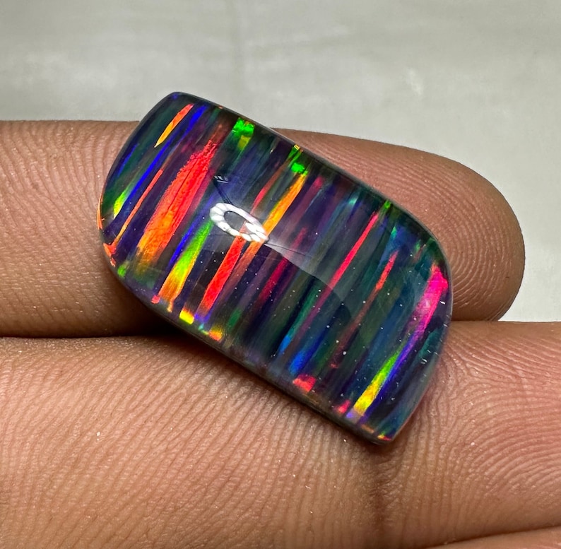 Op de afbeelding: Een zwarte opaal cabochon met een gestreept patroon van iriserende kleuren, waaronder rood, oranje, geel, groen, blauw en paars.