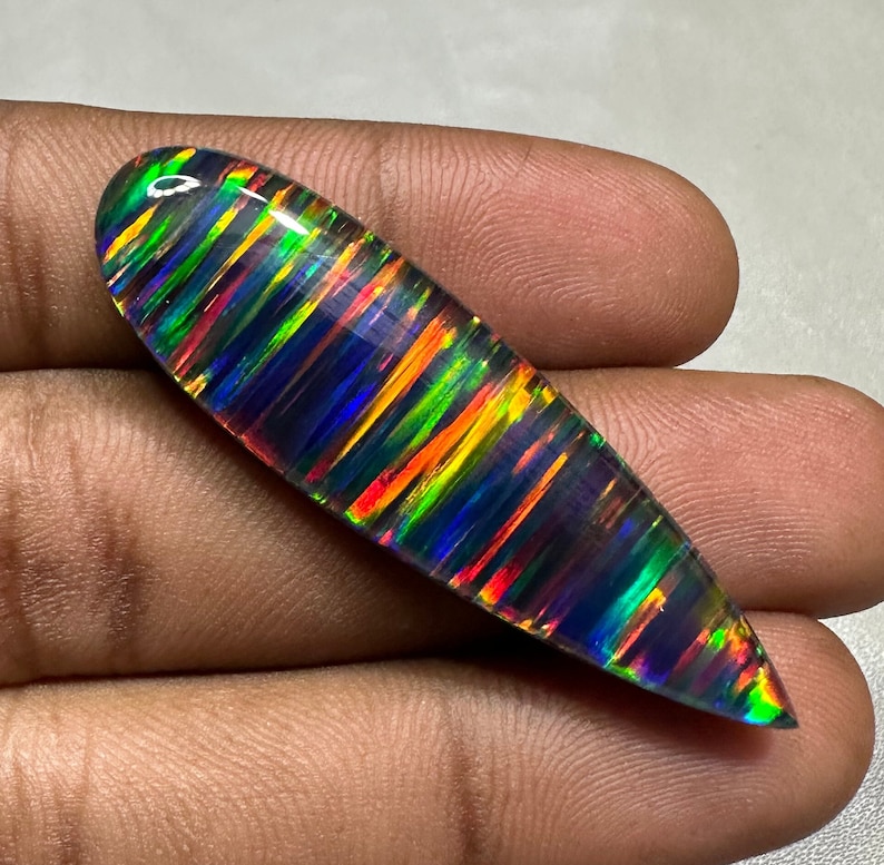 May include: A vibrant, iridescent opal cabochon with a black base and a pattern of colorful stripes. The opal is oval-shaped and has a smooth, polished surface.