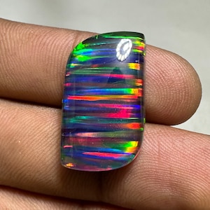 Op de afbeelding: Een zwarte opaal cabochon edelsteen met iriserende regenboogkleuren in een gestreept patroon. De steen is geslepen in een rechthoekige vorm met afgeronde hoeken.