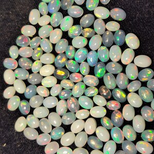 以下が含まれることがあります： 乳白色のベースカラーに、緑、黄色、赤の虹色の輝きが特徴的な、楕円形のオパールのコレクション。宝石は暗い表面に散らばっており、さまざまな色の遊びを見せています。