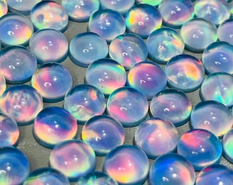 Puede incluir: Una colección de gemas redondas e iridiscentes. Cada piedra muestra una gama de colores, incluyendo azules, rosas y verdes, con un efecto brillante y opalino. Las piedras son lisas y pulidas, probablemente cabujones.