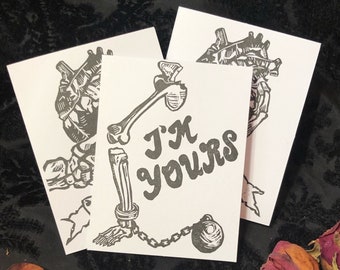 May include: A black and white illustration of a heart with a bone attached to it, with a chain and ball at the end of the bone. The text "I'm yours" is written in a stylised font.
