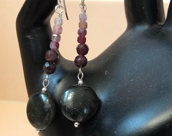 May include: A pair of dangle earrings with a gradient of pink, red and purple gemstone beads. The earrings have a black stone at the bottom.