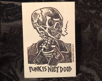 May include: Black and white illustration of a skeleton wearing a leather jacket with studs and smoking a cigarette. The text "PUNK IS NIET DOOD" is below the image.