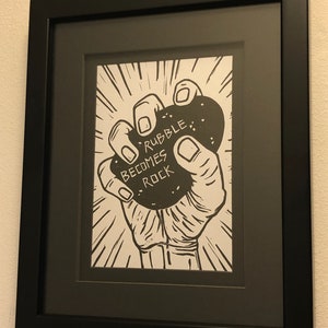Puede incluir: Ilustraci&oacute;n en blanco y negro de una mano sosteniendo una roca con el texto "Rubble Becomes Rock" en ella.