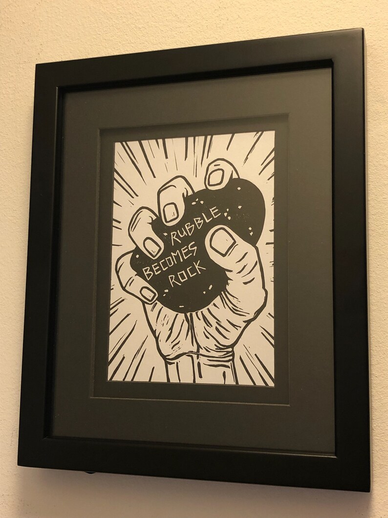 Puede incluir: Ilustraci&oacute;n en blanco y negro de una mano sosteniendo una roca con el texto "Rubble Becomes Rock" en ella.