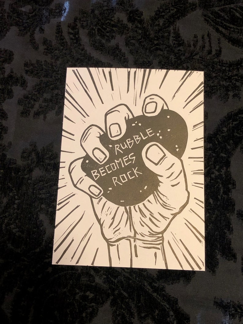 Puede incluir: Una ilustraci&oacute;n en blanco y negro de una mano sosteniendo una roca con el texto "Rubble Becomes Rock" en ella.