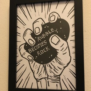 Puede incluir: Ilustraci&oacute;n en blanco y negro de una mano sosteniendo una gran roca con el texto "Rubble Becomes Rock" impreso en ella.