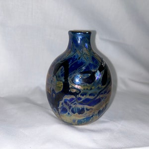 May include: A small, round, iridescent glass vase with a narrow neck. The vase has a blue, black, and gold marbled pattern.