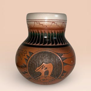 以下が含まれることがあります： 手作りの茶色のセラミック花瓶、クマのデザイン。 花瓶は、薄いベージュの縁、茶色と緑の幾何学模様のバンド、円形のクマのイラストが特徴です。 花瓶の高さは約15cmです。
