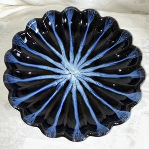 May include: A black and white ceramic bowl with a scalloped edge and a blue and white design. The bowl has a starburst pattern in the center.