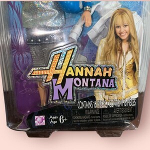 Pu&ograve; includere: Una bambola di Hannah Montana confezionata. La confezione presenta il logo di Hannah Montana e una foto di Miley Cyrus. La confezione contiene 16 pezzi ed &egrave; per bambini dai 6 anni in su. La confezione contiene un avvertimento sui rischi di soffocamento.
