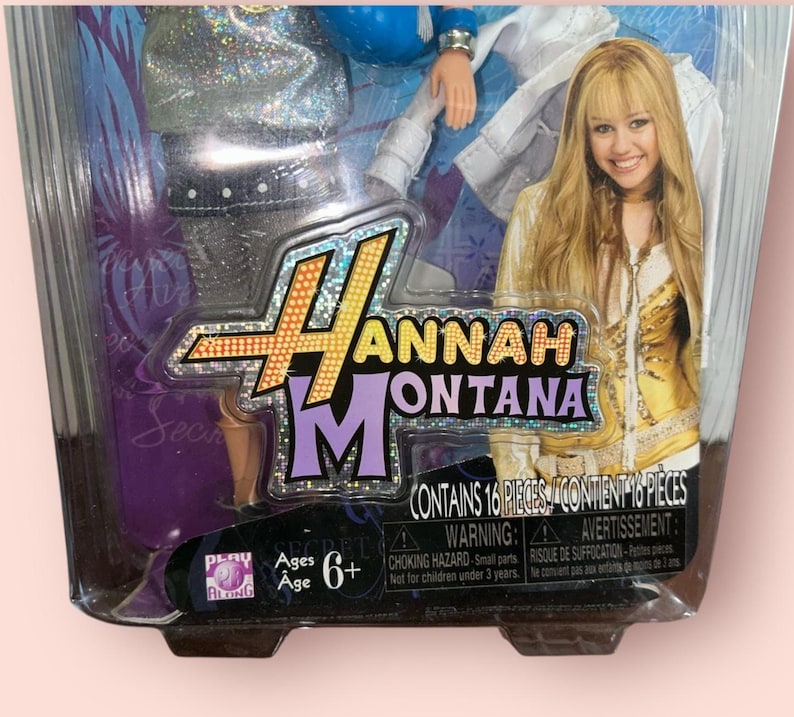 Pu&ograve; includere: Una bambola di Hannah Montana confezionata. La confezione presenta il logo di Hannah Montana e una foto di Miley Cyrus. La confezione contiene 16 pezzi ed &egrave; per bambini dai 6 anni in su. La confezione contiene un avvertimento sui rischi di soffocamento.