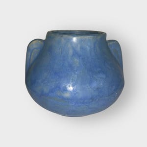 May include: A blue ceramic vase with two curved handles. The vase has a rounded body and a wide opening. The blue color has variations in tone, giving it a textured appearance. The vase is likely handmade.