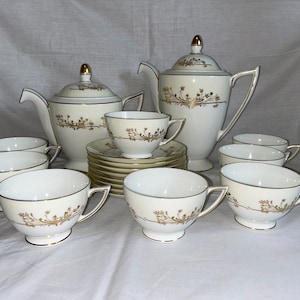 May include: A white tea set with gold floral accents. The set includes a teapot, creamer, sugar bowl, and six cups and saucers.