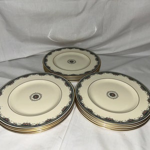May include: A stack of six white dinner plates with a gold rim and a blue and green floral pattern.