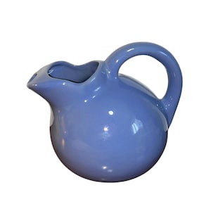 May include: A light blue ceramic jug with a rounded body and a handle. The jug has a smooth, glossy finish.