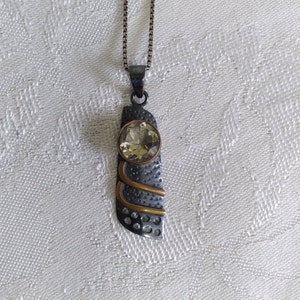 May include: A silver pendant necklace with a textured, geometric design and a large, round, light yellow gemstone.