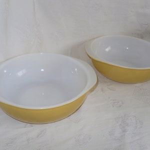 May include: Two yellow mixing bowls with white interiors. The bowls have a rounded shape and a lip around the top edge.