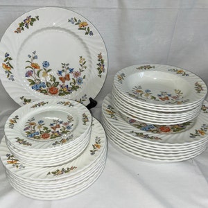 May include: A set of white ceramic dinnerware with a floral pattern featuring butterflies, flowers, and leaves in shades of pink, blue, yellow, and green. The set includes a large dinner plate, a smaller salad plate, and a soup bowl.
