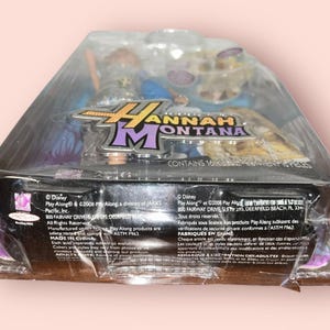 Pu&ograve; includere: Action figure sigillata di Hannah Montana in una confezione di plastica trasparente. La confezione presenta il logo di Hannah Montana in viola e oro. La confezione contiene 16 pezzi. Prodotto da Play Along.