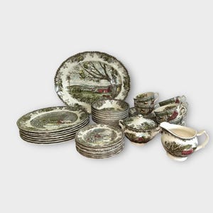 Peut inclure: Service de table en porcelaine vintage avec un motif de paysage champêtre dans les tons de vert, marron et rouge. L'ensemble comprend des assiettes, des bols, des tasses, des soucoupes, un sucrier, une crémière et un plat de service.