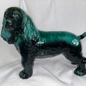 May include: A green glazed ceramic figurine of a black cocker spaniel dog. The dog is standing with its head turned to the side and its tail curled.
