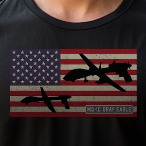 May include: Black t-shirt featuring an American flag design with silhouettes of military aircraft. The flag has a distressed look. The text "MQ-1C GRAY EAGLE" is below the flag.