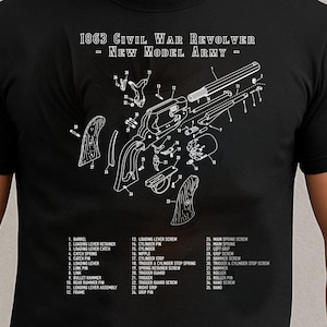 Może przedstawiać: Czarny t-shirt z białym diagramem rewolweru z wojny secesyjnej z 1863 roku, ze szczegółowymi, opisanymi częściami. Tekst "1863 Civil War Revolver - New Model Army" jest wydrukowany nad diagramem. Koszulka jest noszona przez osobę.