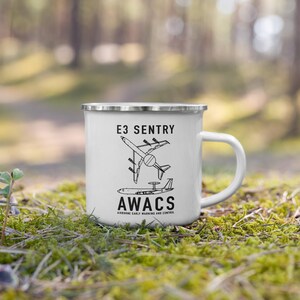 Puede incluir: Taza de esmalte blanco con borde y asa plateados. La taza presenta el texto "E3 SENTRY" sobre una ilustración negra de un avión, con "AWACS" y "AIRBORNE EARLY WARNING AND CONTROL" debajo.