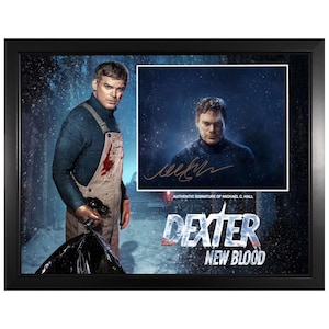 May include: Framed artwork featuring Michael C. Hall from "Dexter: New Blood." The image shows Hall in character, with a signature and the show's logo. The artwork is set against a snowy backdrop, framed in black.