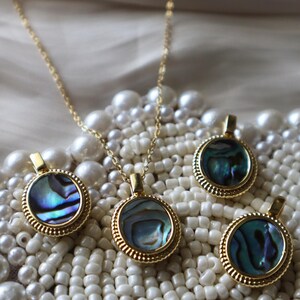 May include: A gold-toned necklace and three matching pendants, each featuring a circular abalone shell inlay with iridescent blue, green, and purple hues. The pendants are framed by a textured, ridged gold-toned metal border with a small bail.