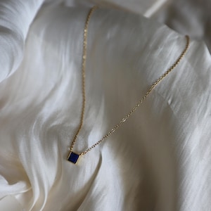 Peut inclure: Un collier en cha&icirc;ne dor&eacute;e avec un petit pendentif carr&eacute; en pierre bleue.