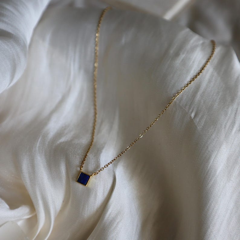 Peut inclure: Un collier en cha&icirc;ne dor&eacute;e avec un petit pendentif carr&eacute; en pierre bleue.