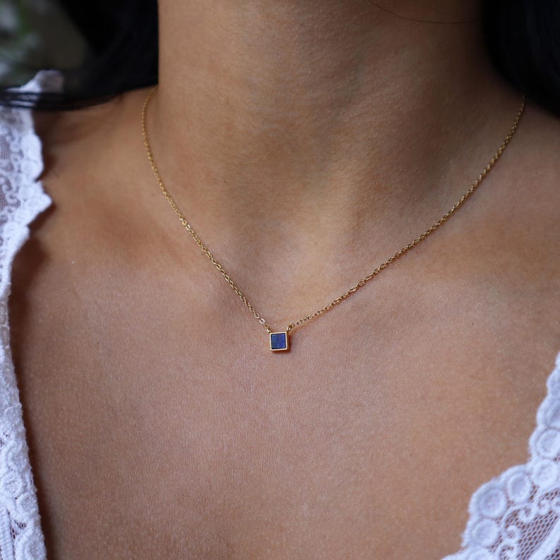 Peut inclure: Un collier en cha&icirc;ne dor&eacute;e avec un petit pendentif carr&eacute; orn&eacute; d'une pierre bleu fonc&eacute;.