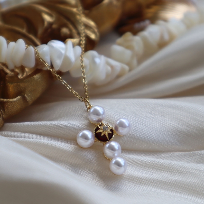 Puede incluir: Un collar de oro con un colgante de cruz de perlas. La cruz tiene un centro rojo con una peque&ntilde;a estrella y est&aacute; rodeada de cinco perlas.