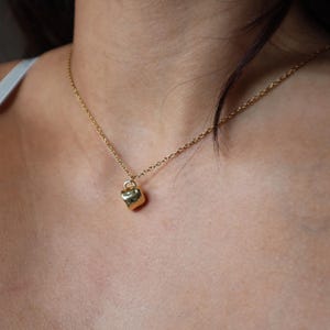 May include: A gold chain necklace with a small, textured, gold heart pendant.