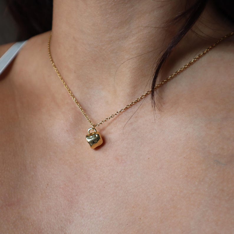 May include: A gold chain necklace with a small, textured, gold heart pendant.